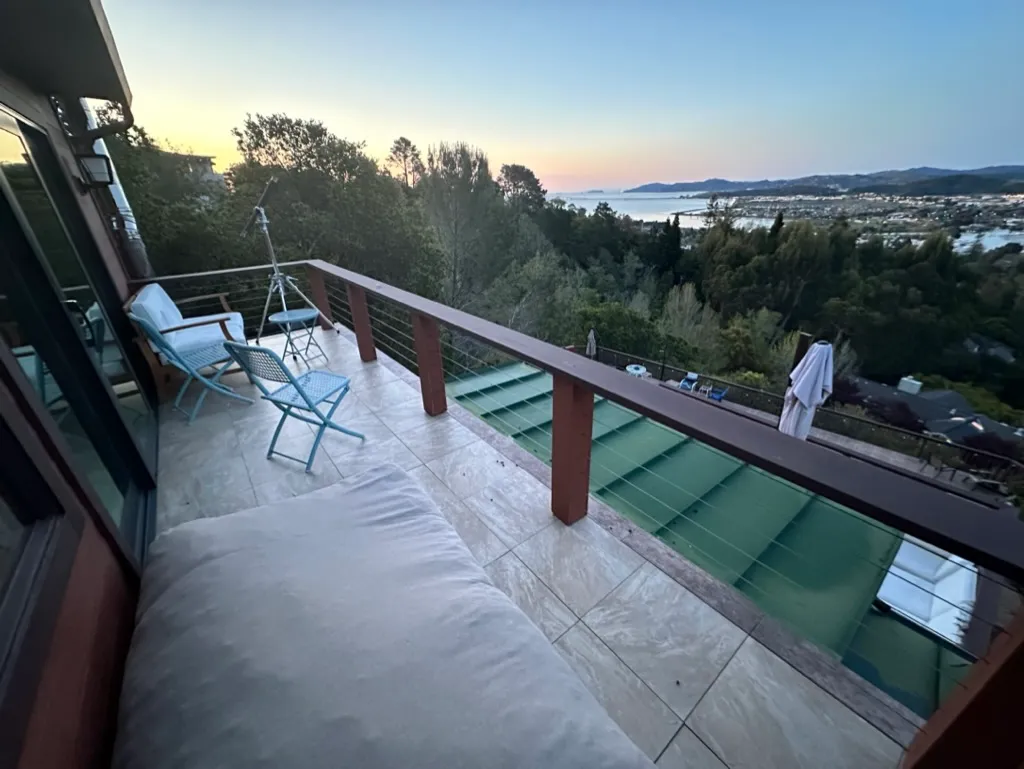A tiled deck with chairs and a daybed cushion looking out over the bay at dusk