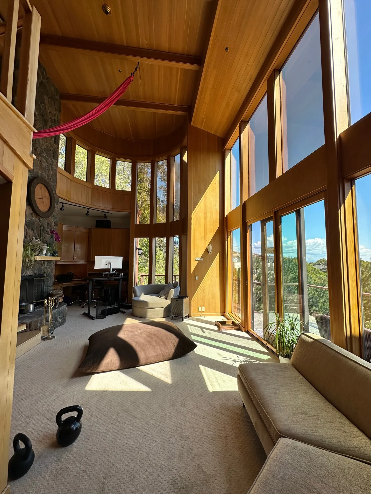 The great room under a vaulted cedar ceiling with red aerial silks and a stone fireplace