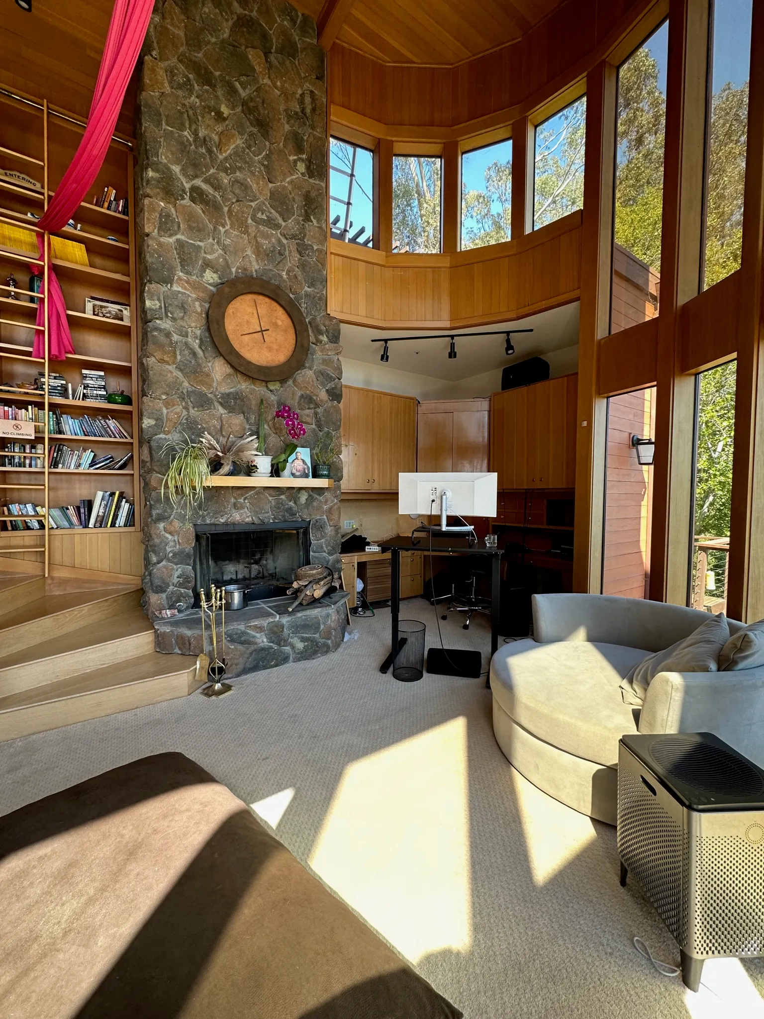 A double-height library with a river-rock fireplace, tall bookshelves, and hanging aerial silks
