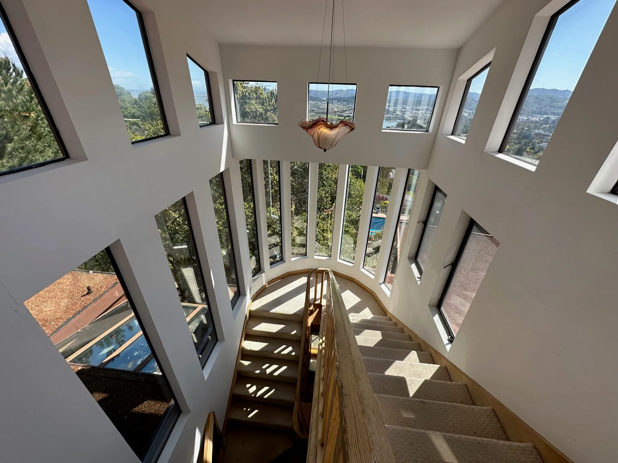 A bright geometric stairwell wrapped in angled windows with a blown-glass pendant light
